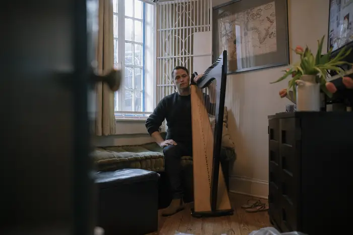 A person sits, in their apartment, beside their harp.